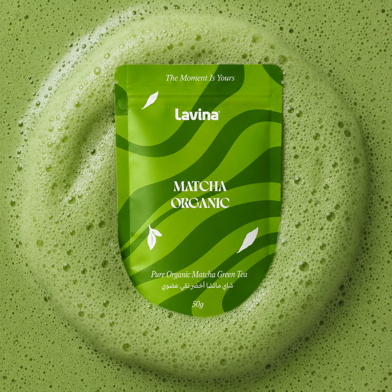 A green stand-up pouch of Lavina Matcha Organic green tea centered on a matching green foamy surface with visible bubbles.