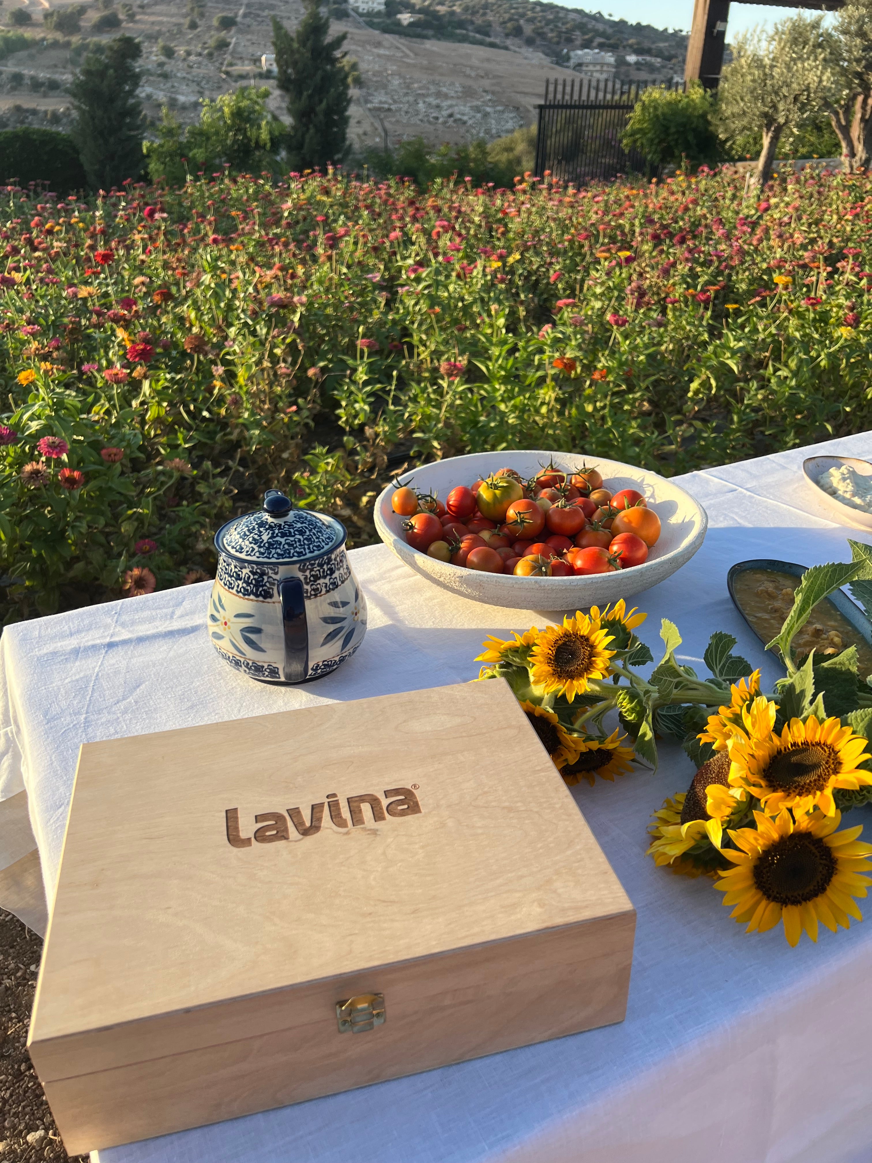 Outdoor setting with a wooden box labeled 'Lavina', sunflowers, and strawberries on a tablecloth.