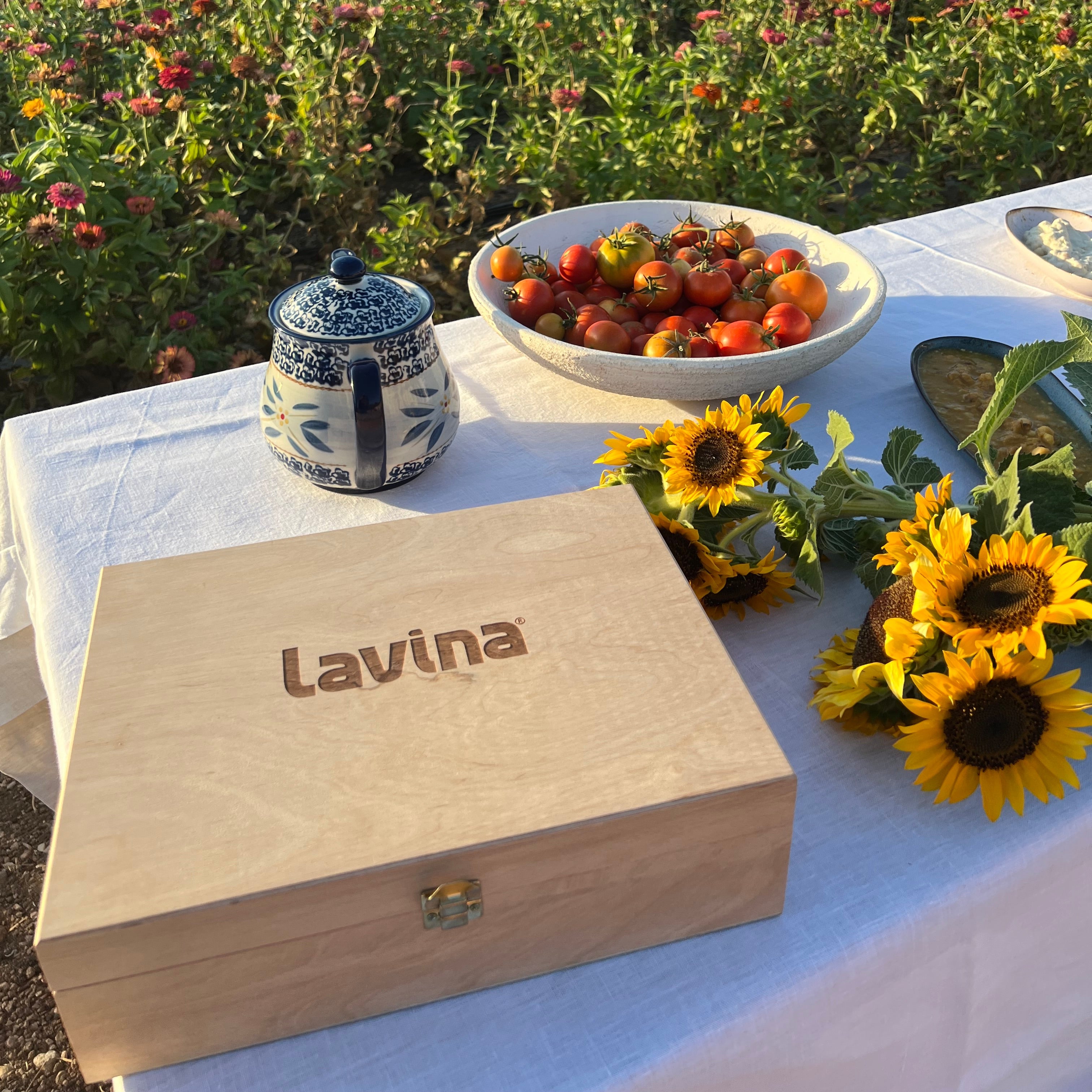 Outdoor setting with a wooden box labeled 'Lavina', sunflowers, and strawberries on a tablecloth.