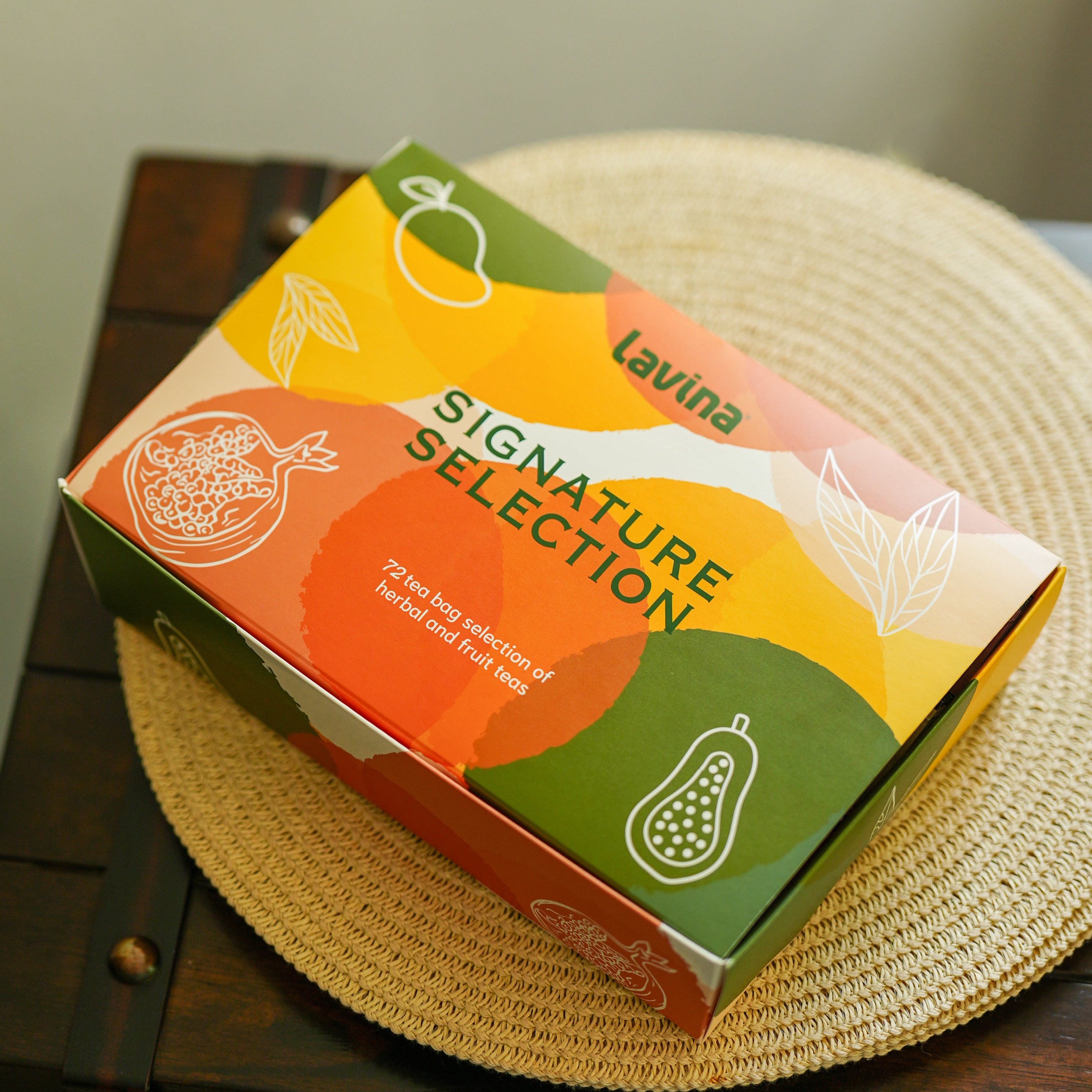 Lavina Signature Selection product box resting on a woven straw placemat over a dark wooden table.