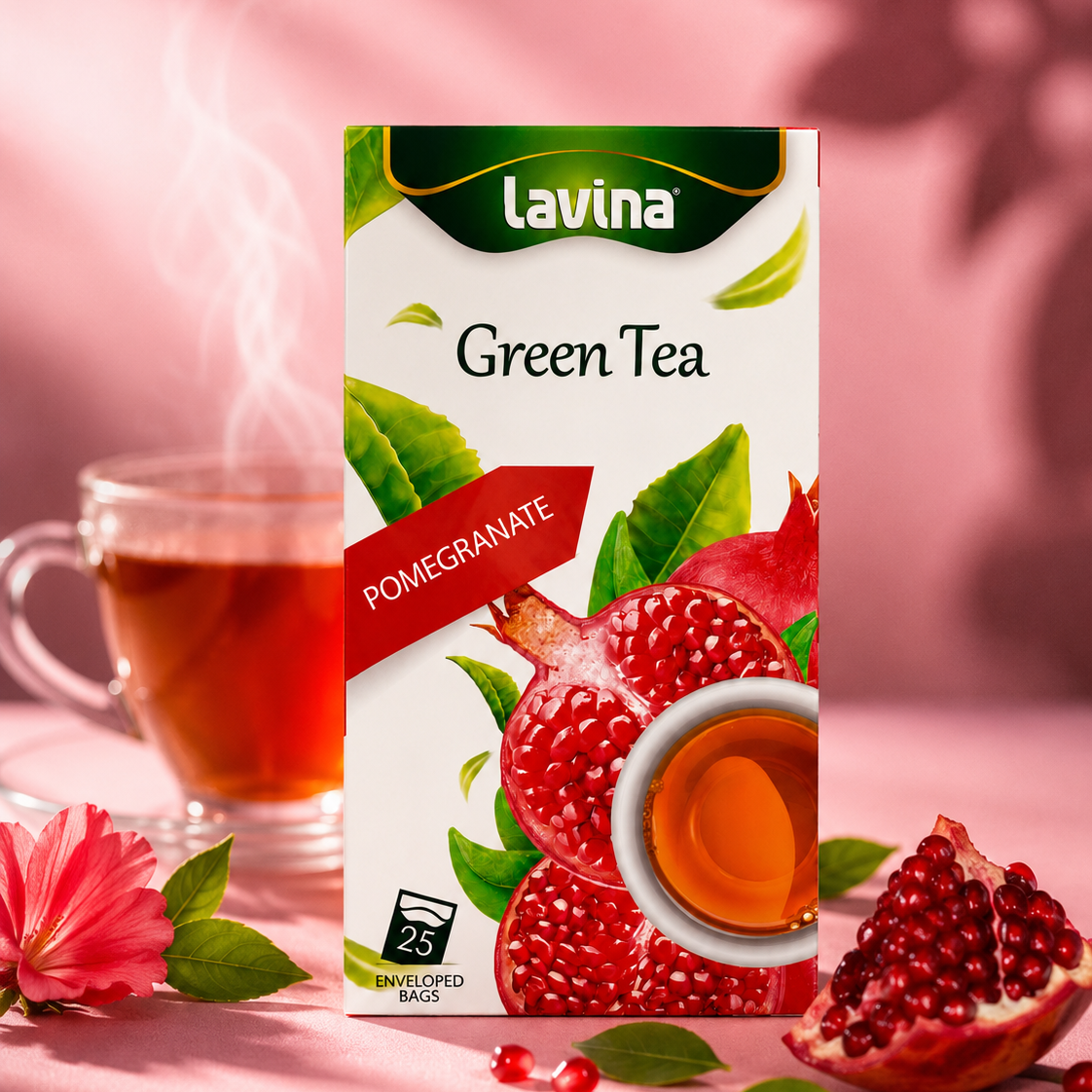 A box of Lavina Green Tea Pomegranate flavor stands on a pink surface with a glass cup of tea, pomegranate halves, leaves, and flowers around it. The box shows the Lavina brand and features illustrations of pomegranate and green tea leaves.